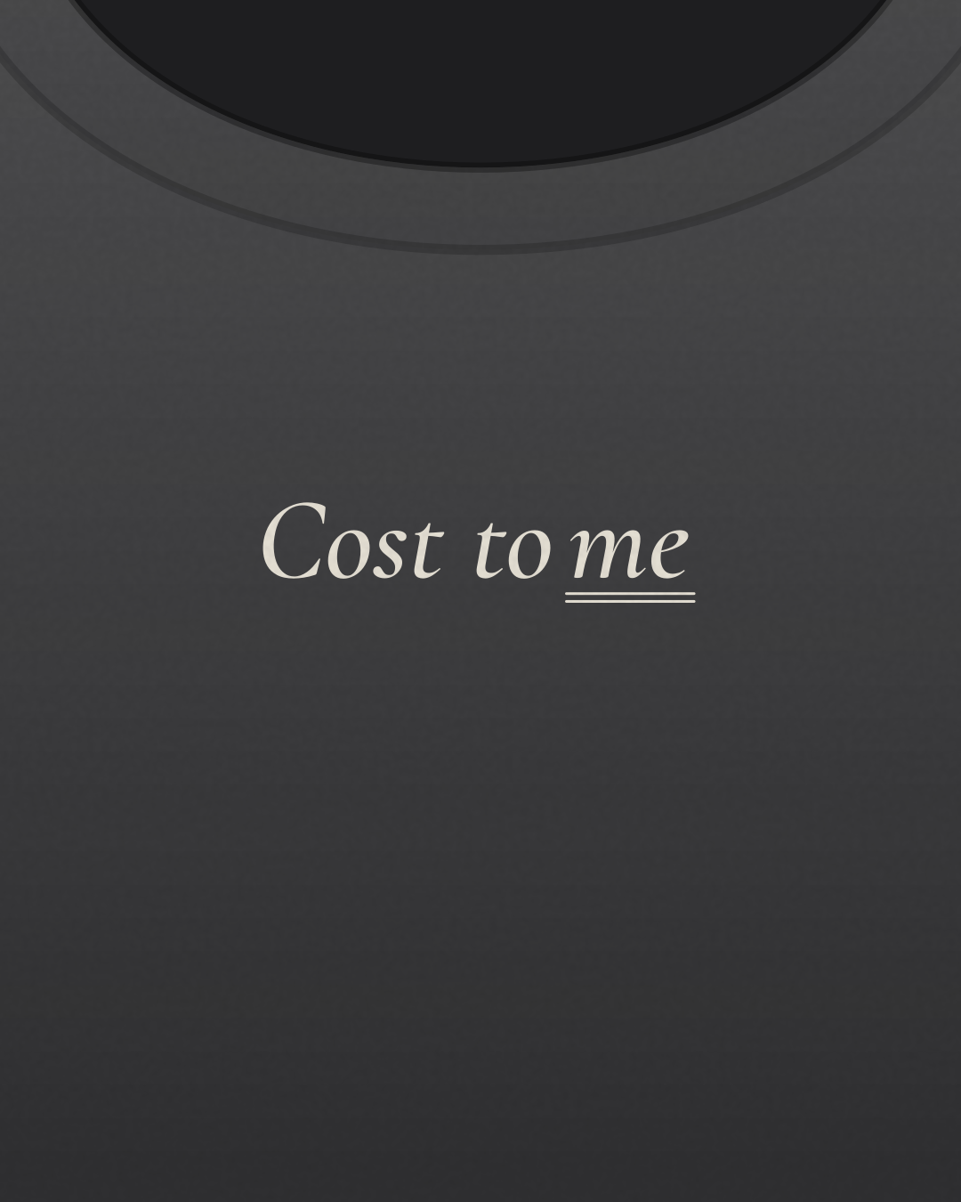 Close-up of the “Cost to me” print in cream on a charcoal tee