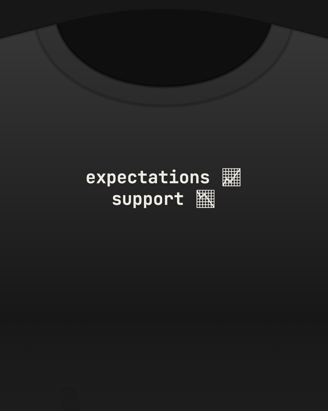 Close-up of a black tee with “expectations 📈 support 📉” printed small in off-white on the chest